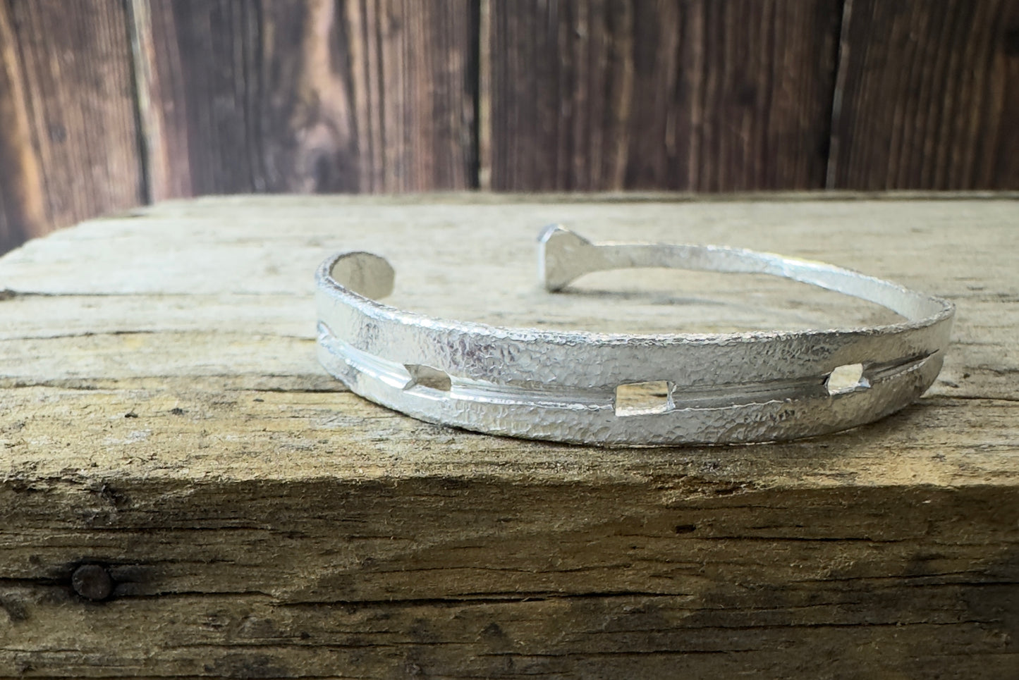 A silver cuff bracelet Hand forged to resemble a horseshoe with a textured surface, displayed on a wooden surface.
