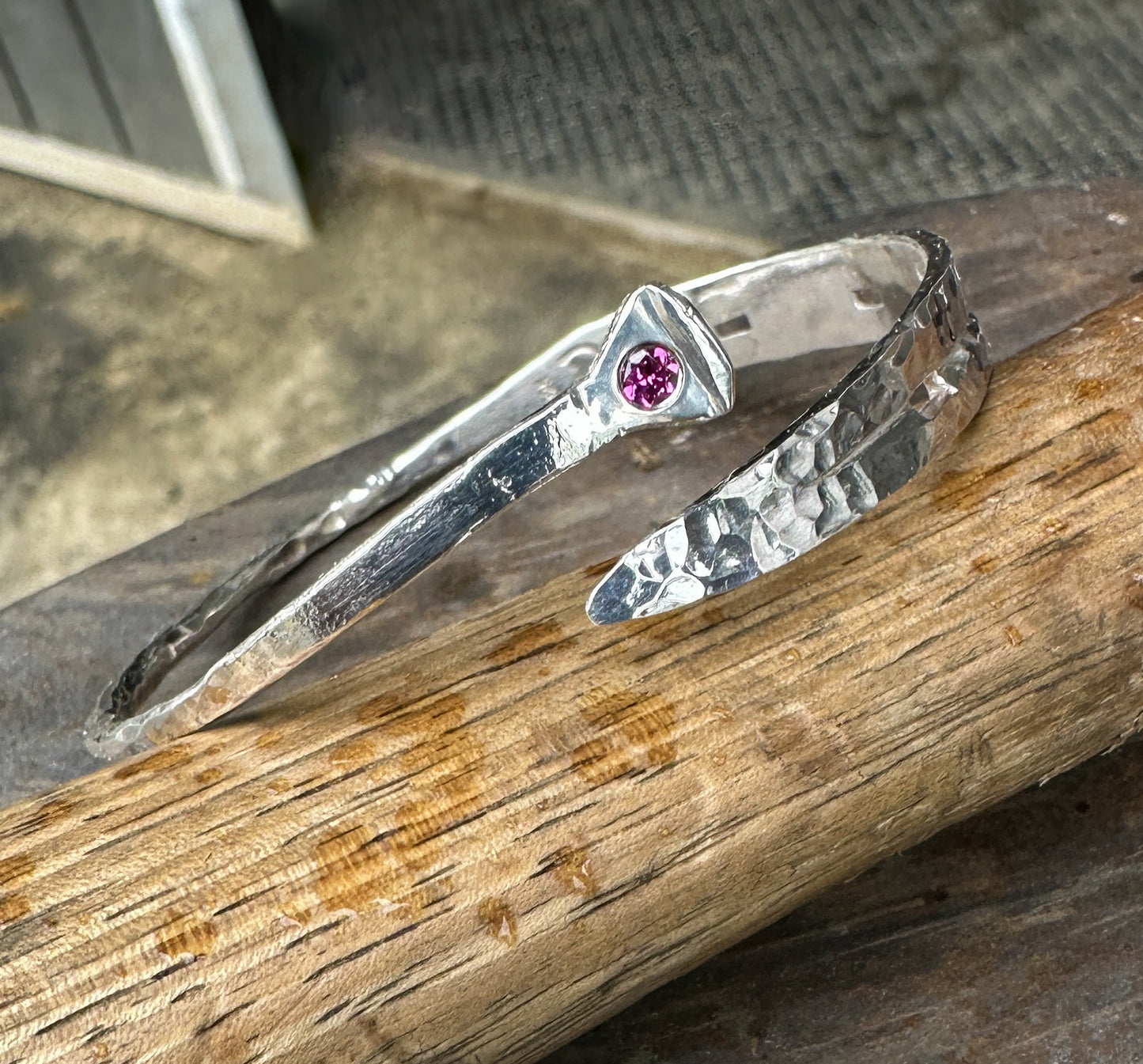 Sterling silver cuff bracelet hand-forged in the shape of a horseshoe. Features a sandcast horseshoe nail with pink Rhodolite Garnet