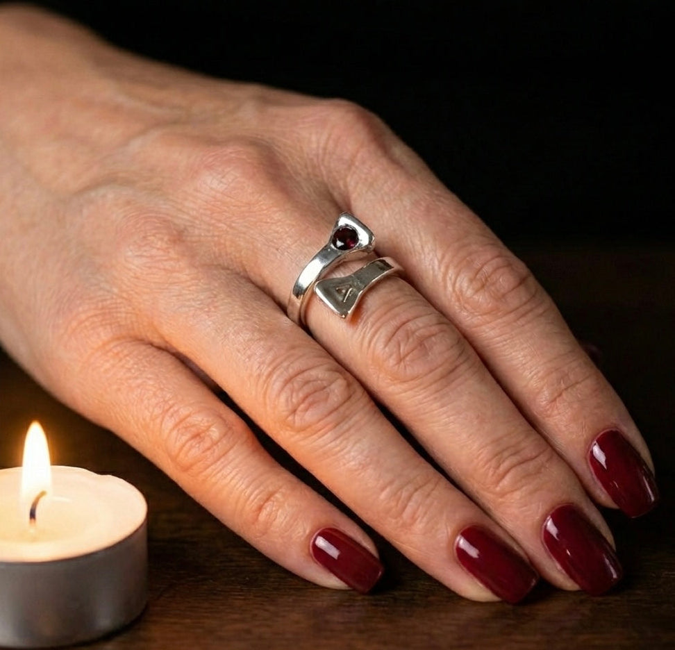 Hand with a silver ring featuring a red gemstone, next to a lit candle on a dark background