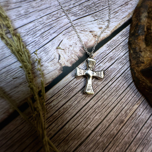 Small horseshoe nail cross pendant. Displayed against a rustic wood background