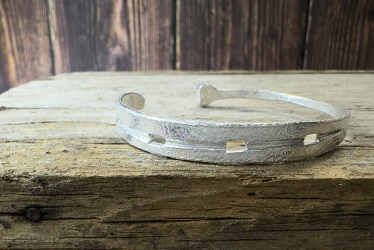A silver cuff bracelet Hand forged to resemble a horseshoe with a textured surface, displayed on a wooden surface.