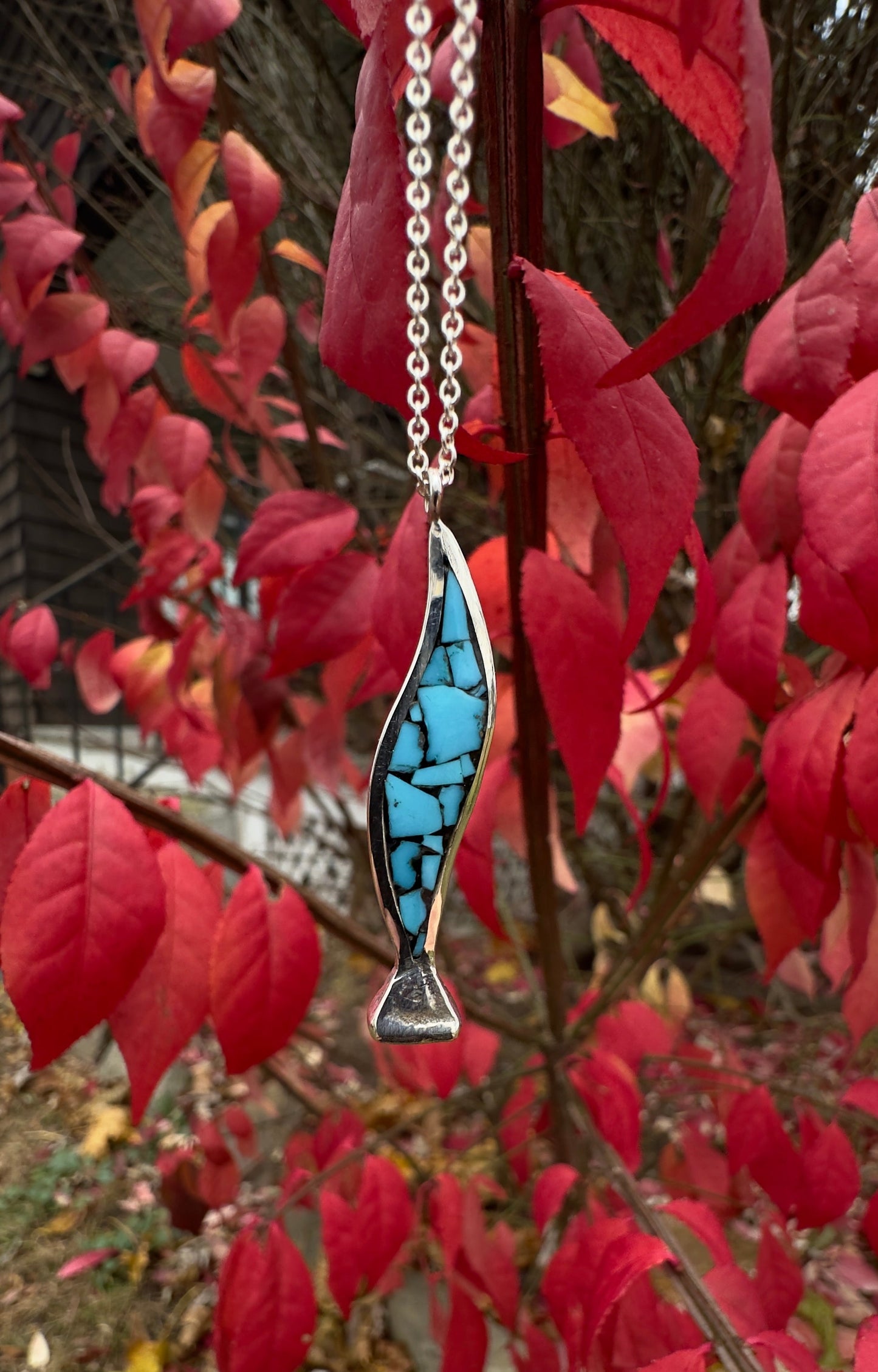 decorative silver and turquoise horseshoe nail pendant against red leaves